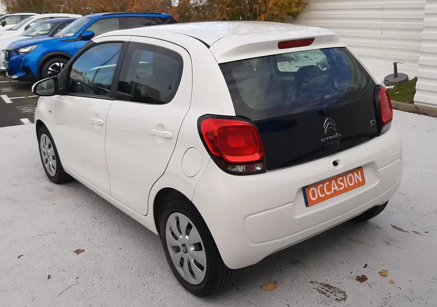 Vue 3/4 arrière droite d'une Citroën C1 blanche 5 portes avec vitres arrière teintées et plaque "OCCASION" orange.