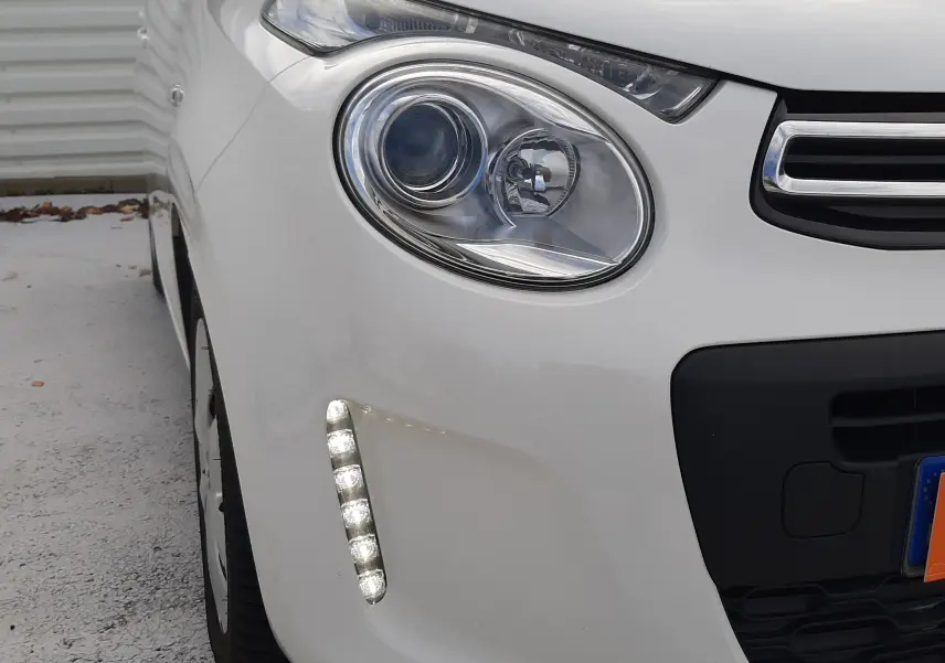 Gros plan sur le phare avant gauche blanc d'une Citroën C1 2021 avec feux LED diurnes allumés.