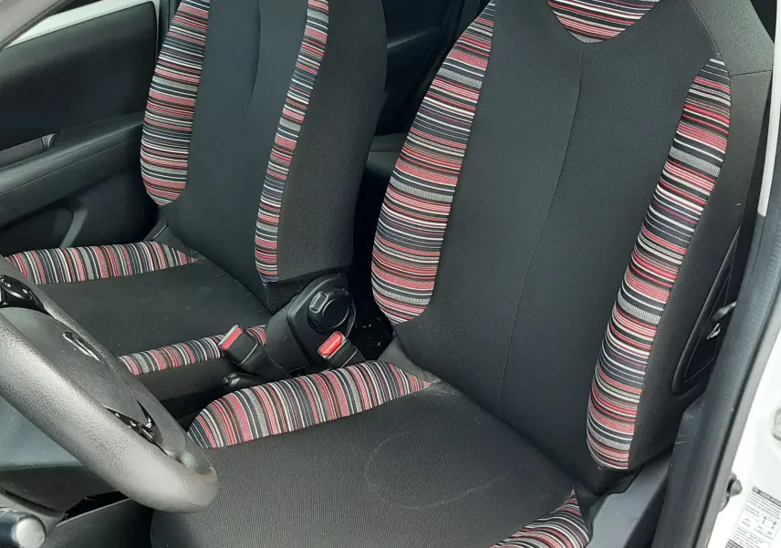 Vue intérieure côté gauche montrant les sièges avant en tissu noir avec motifs rayés rouges et gris d'une Citroën C1 blanche 2021.