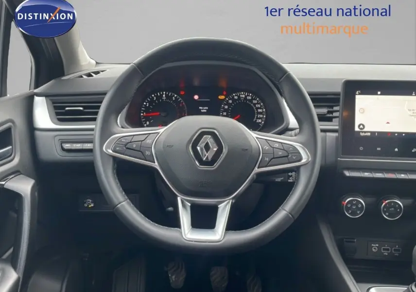 Vue intérieure centrée sur le volant Renault Captur gris cassiopée, tableau de bord et écran tactile en arrière-plan.