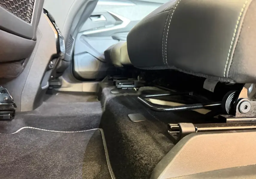 Vue en contre-plongée sous les sièges arrière du Peugeot 5008 Hybrid 145 GT, montrant la moquette noire et les rails de fixation.