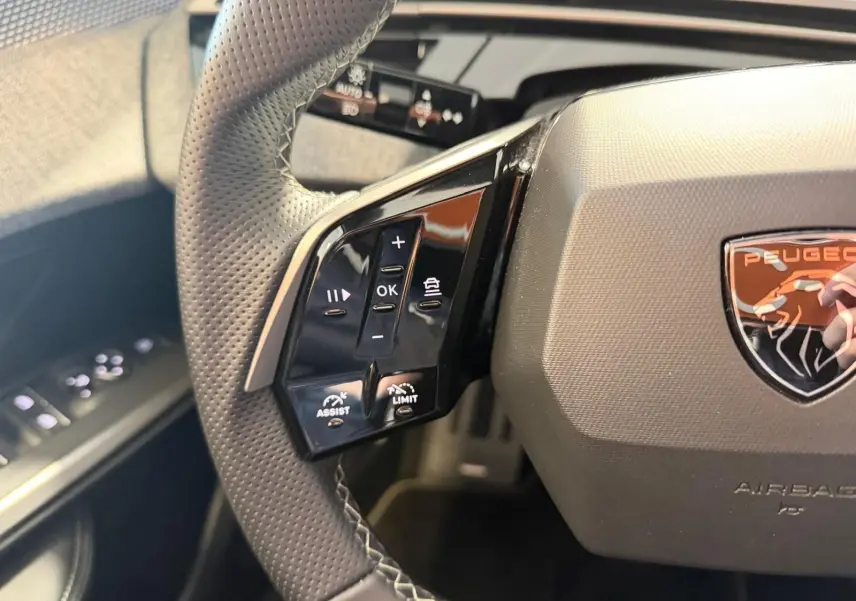 Gros plan sur le volant perforé du Peugeot 5008 Hybrid 145 GT avec commandes d’assistance et logo lion orange.