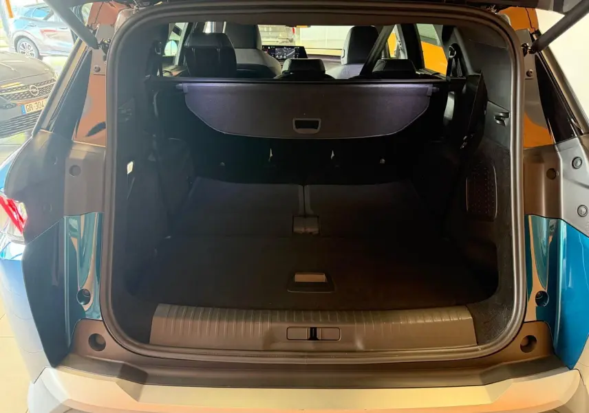 Coffre ouvert vu de l'arrière du Peugeot 5008 Hybrid 145 bleu obsession avec toit noir dans un showroom.