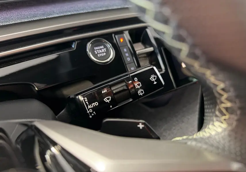 Détail intérieur du Peugeot 5008 Hybrid 145 GT montrant la commande d’essuie-glace et le bouton start/stop, avec surpiqûres jaunes visibles.