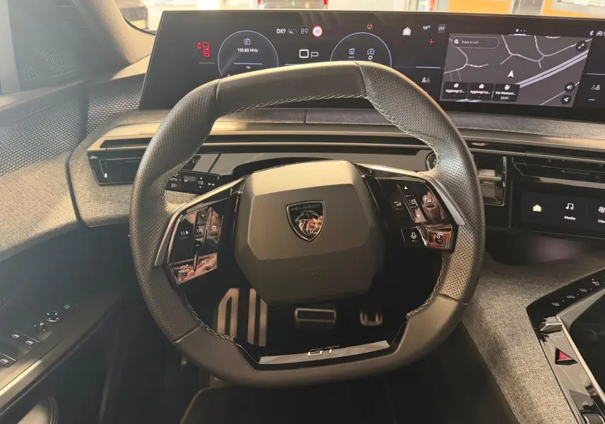 Vue intérieure centrée sur le volant GT du Peugeot 5008 Hybrid 145, avec tableau de bord numérique et écran GPS panoramique.
