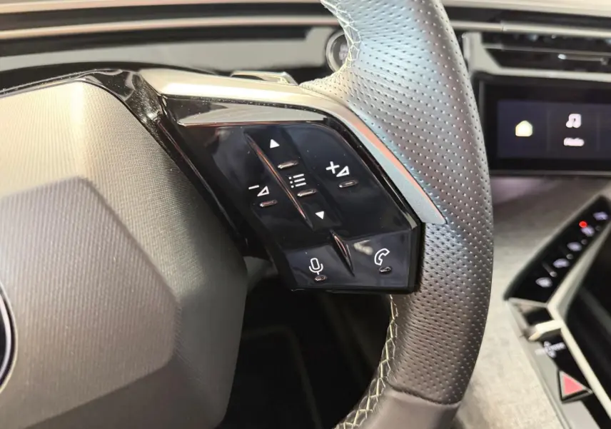 Gros plan sur le volant perforé côté gauche du Peugeot 5008 Hybrid 145 GT, avec commandes vocales et téléphone.