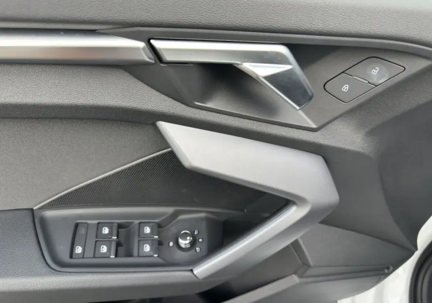 Détail de la porte avant gauche de l’Audi A3 2024 blanche, montrant les commandes de vitres et la poignée intérieure argentée.