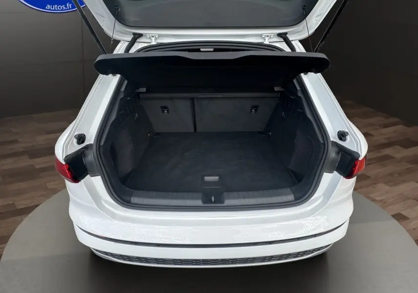 Coffre ouvert vu de l'arrière d'une Audi A3 blanche 2024, mettant en valeur l'espace de chargement intérieur noir.
