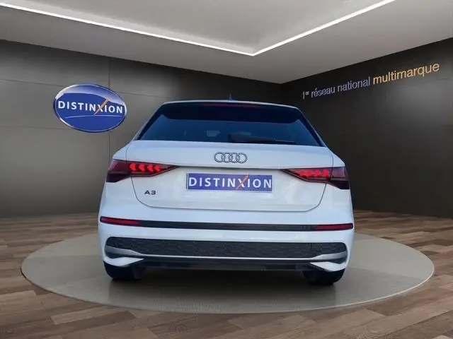Vue arrière d'une Audi A3 blanche 2024, avec feux LED allumés et logo Distinxion en arrière-plan.