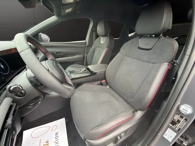 Vue intérieure côté conducteur du Hyundai Tucson 1.6 Hybrid gris foncé, sièges en alcantara avec surpiqûres rouges et volant cuir perforé.