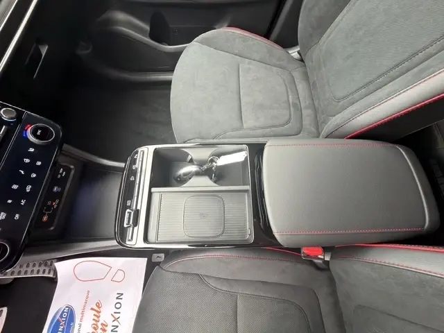 Vue intérieure centrée sur la console centrale et accoudoirs gris foncé avec surpiqûres rouges du Hyundai Tucson 2026.