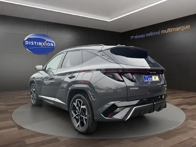 Vue 3/4 arrière droite d’un Hyundai Tucson gris foncé avec hayon motorisé et jantes alliage distinctives en showroom.
