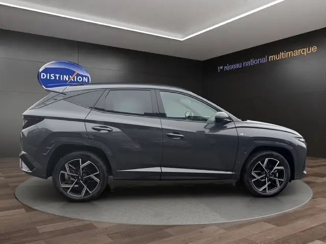 Profil côté gauche d'un Hyundai Tucson 1.6 Hybrid N Line Creative gris foncé avec jantes alliage et hayon motorisé en showroom.