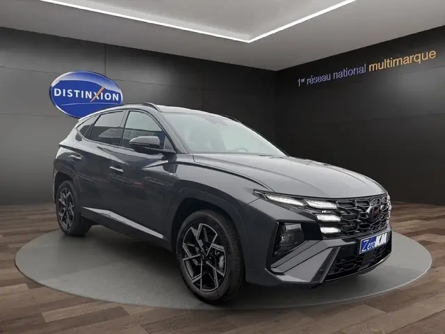 Vue 3/4 avant d’un Hyundai Tucson gris foncé avec calandre distinctive et jantes alliage noires, en showroom.