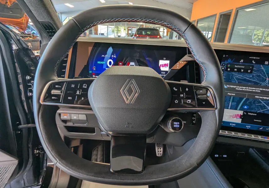 Vue rapprochée du volant noir avec surpiqûres bleues du Renault Espace VI E-Tech, écran numérique et tableau de bord visible.