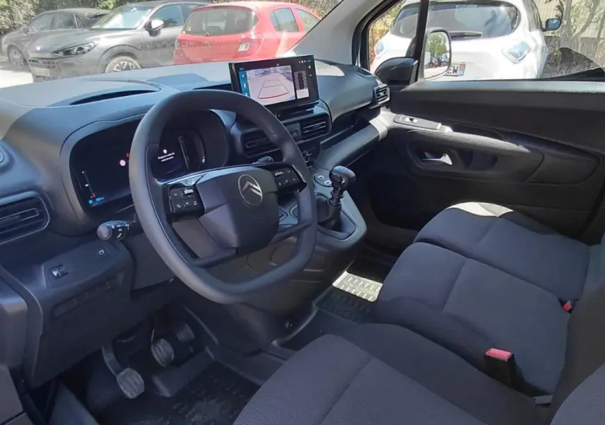 Intérieur avant droit du Citroën Berlingo blanc 2025, volant multifonctions, écran tactile et sièges tissu gris.