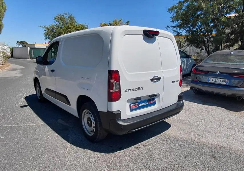 Vue 3/4 arrière droite d’un Citroën Berlingo blanc utilitaire avec porte latérale, garé sur une route ensoleillée.