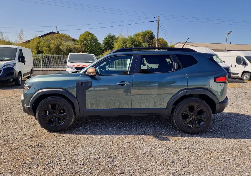 Vue de profil droit du Dacia Duster 1.8 Hybrid 155 Extreme vert cèdre avec jantes noires et coques de rétroviseur bronze.