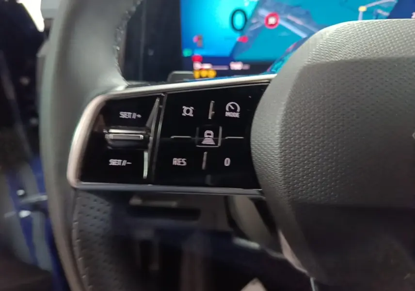 Gros plan sur les commandes du volant cuir côté gauche du Renault Austral bleu, avec écran numérique en arrière-plan.