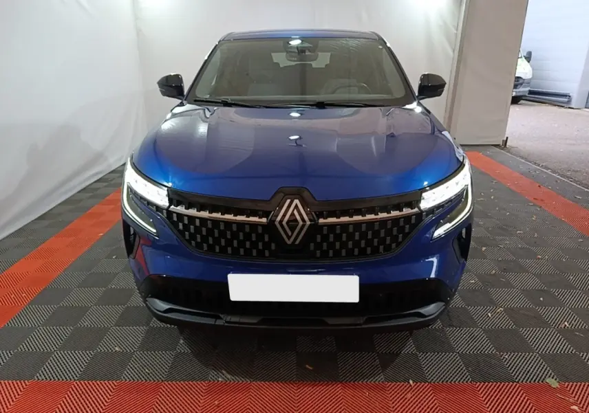 Vue frontale d'un Renault Austral bleu 2024 avec calandre noire et phares LED allumés dans un espace fermé.