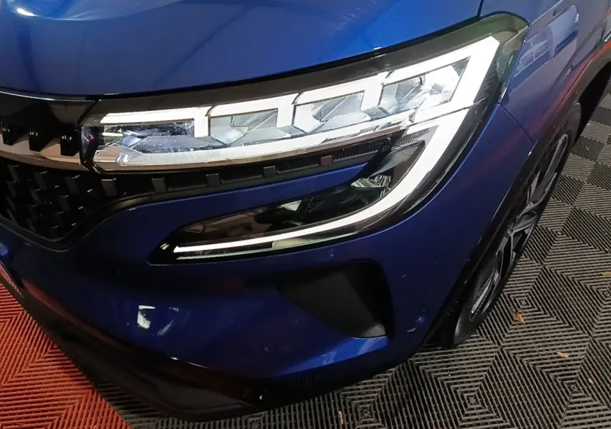 Gros plan sur l'avant droit bleu du Renault Austral 2024, mettant en valeur le phare LED et la calandre distinctive.