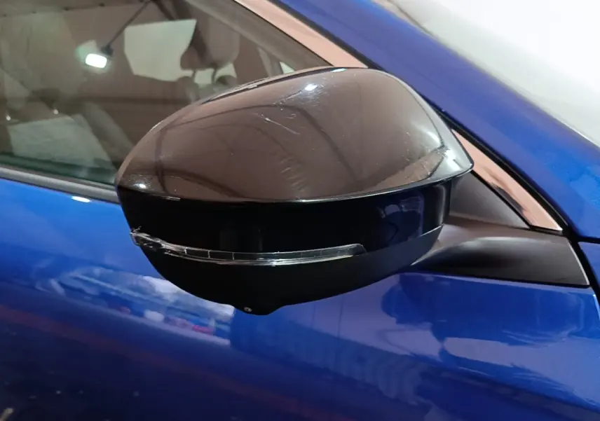 Rétroviseur noir en gros plan côté gauche d’un Renault Austral bleu 2024, avec clignotant intégré.
