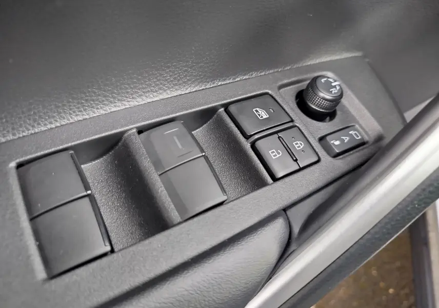 Gros plan sur les commandes de lève-vitres et réglage des rétroviseurs côté conducteur du Toyota Corolla Cross gris acier 2025.