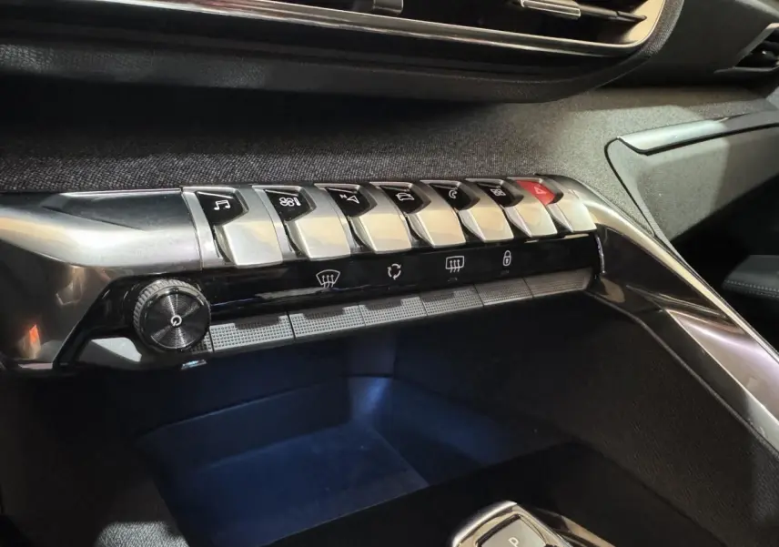 Gros plan sur la console centrale noire du Peugeot 3008 PureTech 130, mettant en valeur les boutons métalliques et commandes.