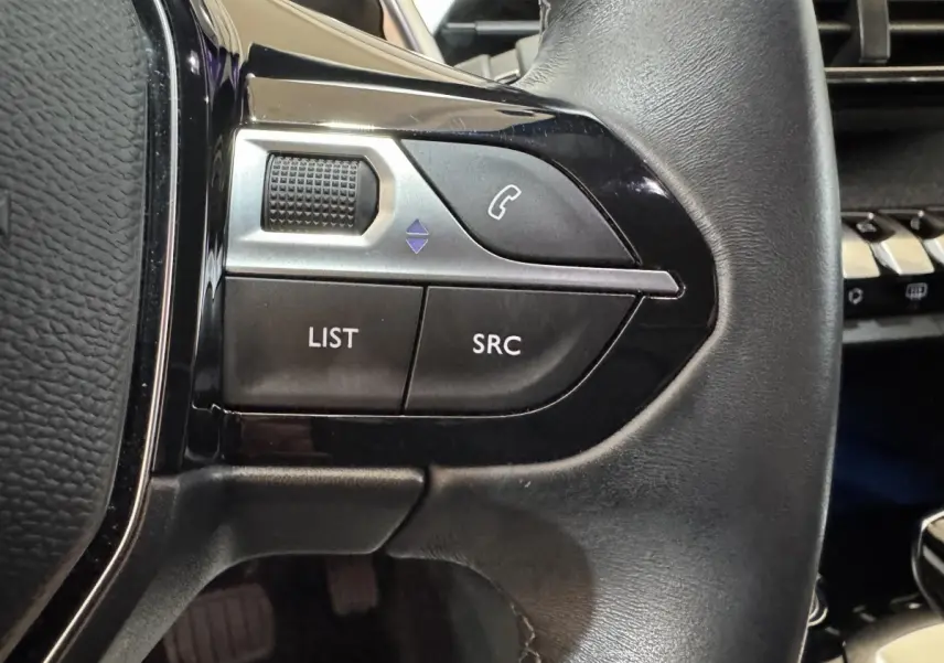 Gros plan sur les commandes gauche du volant noir du Peugeot 3008 orange, avec boutons téléphone et liste.