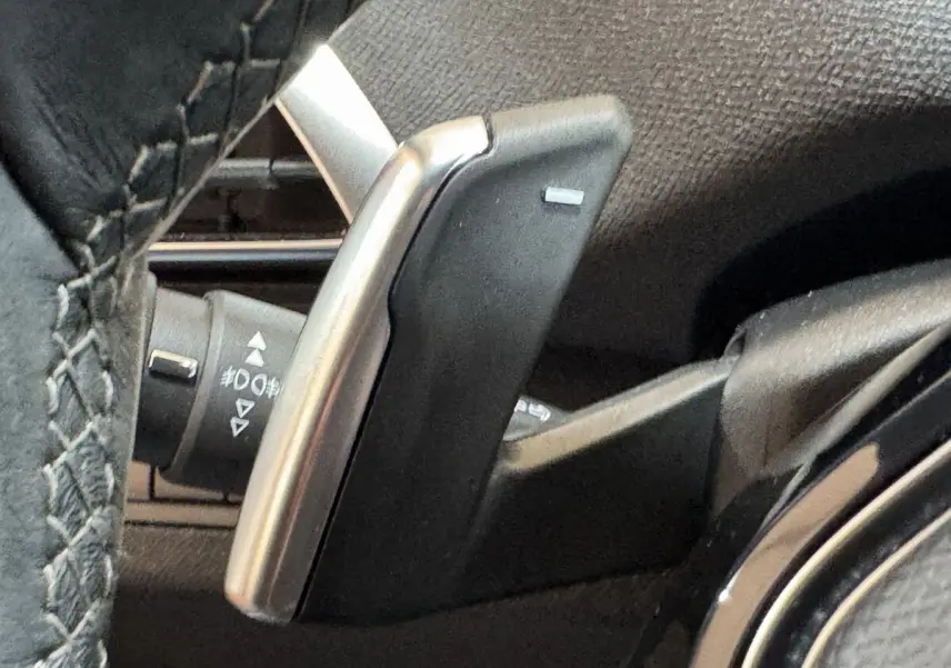 Gros plan sur la palette de changement de vitesse en aluminium et plastique noir, côté gauche du volant cuir du Peugeot 3008 orange.