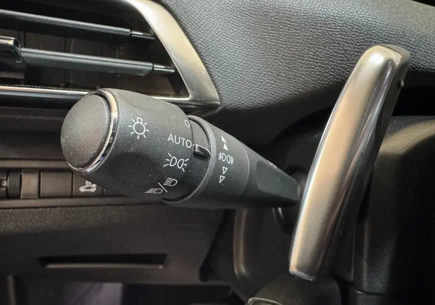 Gros plan sur la commande des phares à gauche du volant dans l’habitacle noir du Peugeot 3008 orange 2020.