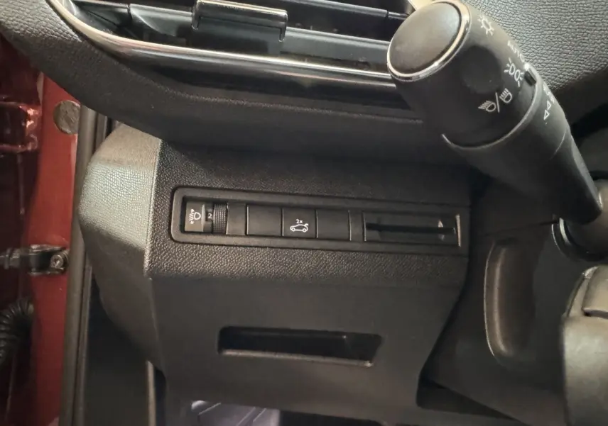 Détail intérieur côté gauche du tableau de bord noir avec commandes d’éclairage et ouverture du coffre, bord orange visible.