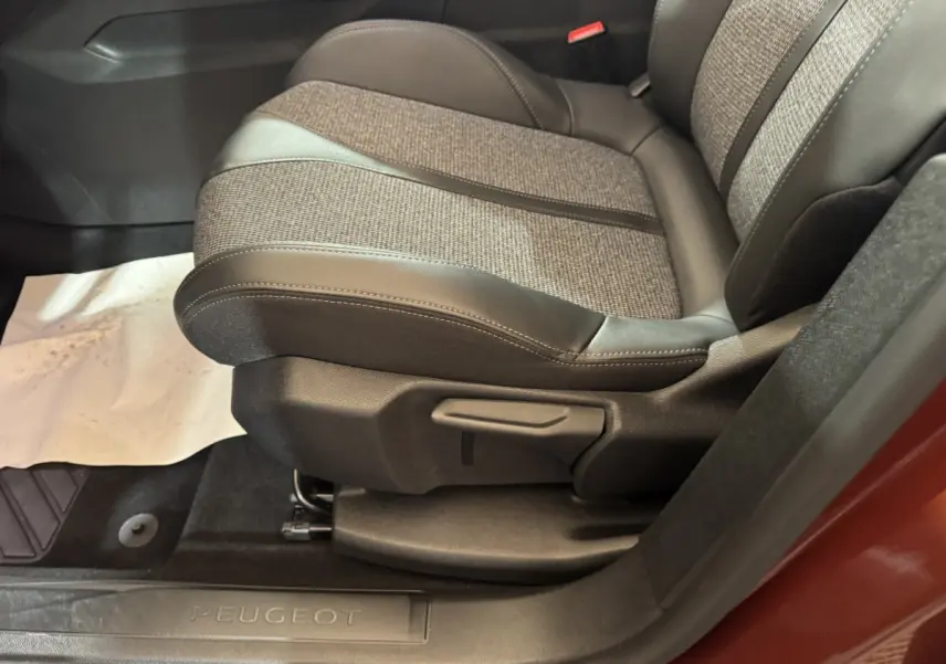 Gros plan sur le siège avant droit tissu et cuir gris d’un Peugeot 3008 orange, avec seuil de porte marqué Peugeot.