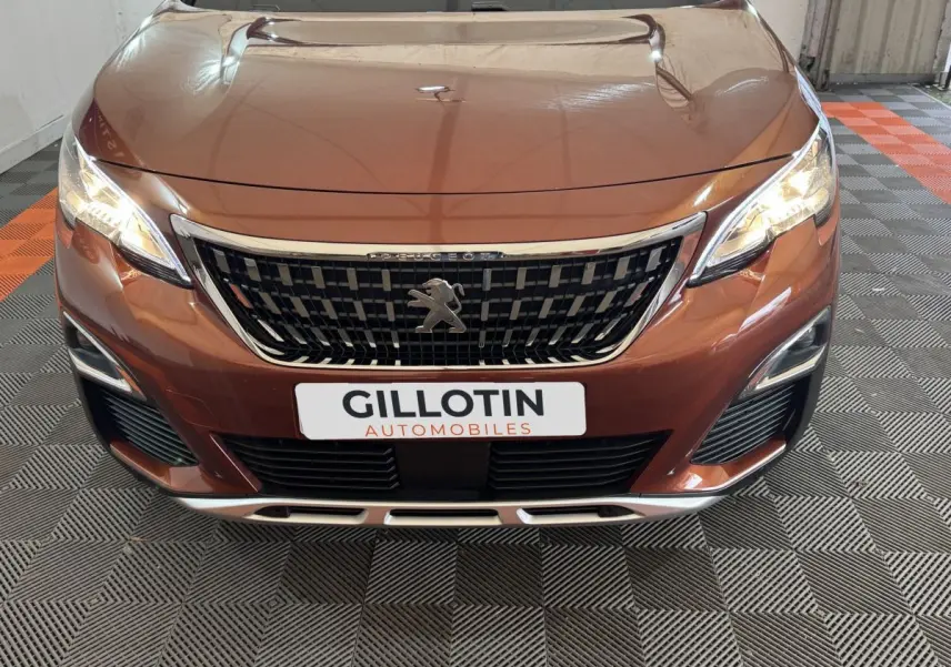 Vue avant rapprochée du Peugeot 3008 orange 2020 avec calandre chromée et phares LED allumés.