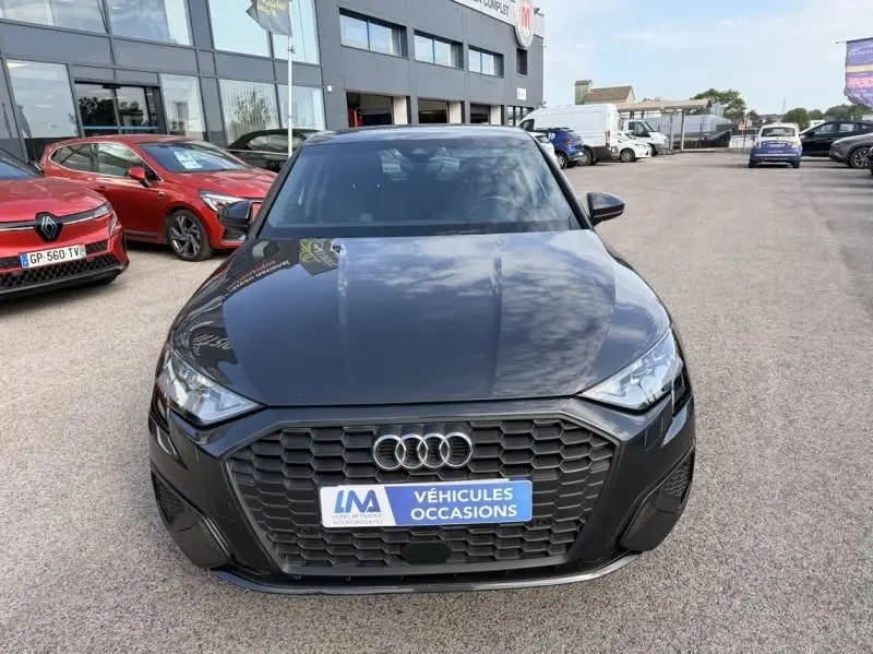 Vue avant d'une Audi A3 Berline gris foncé métal 2022 avec calandre hexagonale et plaque "Véhicules Occasions" sur un parking.