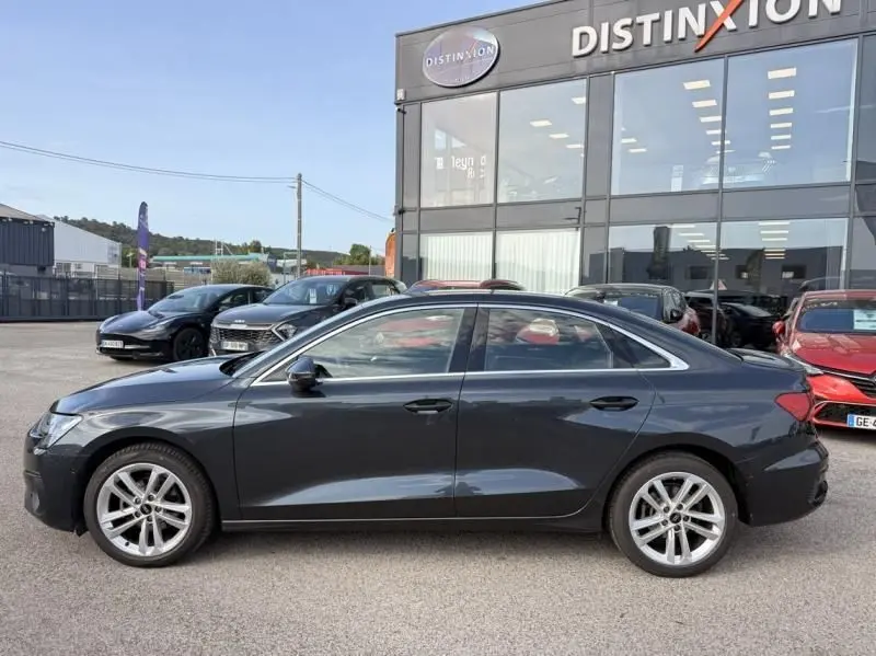 Audi A3 Berline 35 TFSI gris foncé métal vue de profil côté gauche, garée devant un showroom Distinxion.
