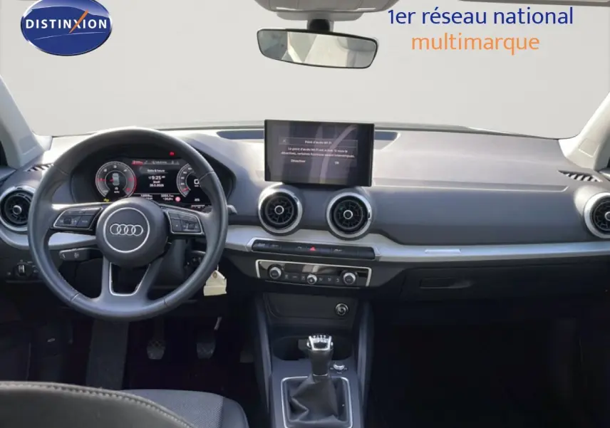 Vue intérieure avant de l'Audi Q2 30 TDI S-Line 2025, tableau de bord gris avec volant cuir et boîte manuelle.