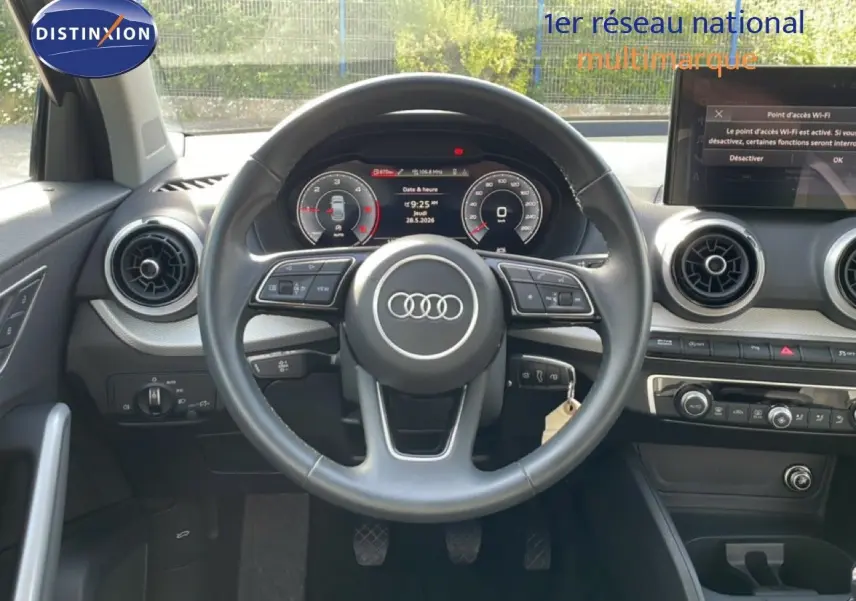 Vue frontale de l'intérieur de l'Audi Q2 30 TDI S-Line 2025, volant cuir noir et tableau de bord digital.