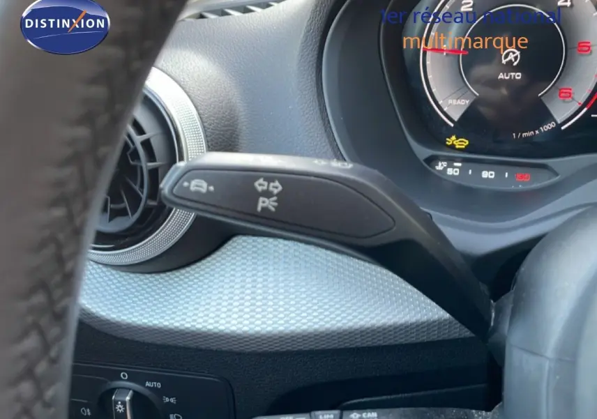 Gros plan sur la commande de clignotant à gauche du volant d’un Audi Q2 gris Manhattan, tableau de bord numérique visible.