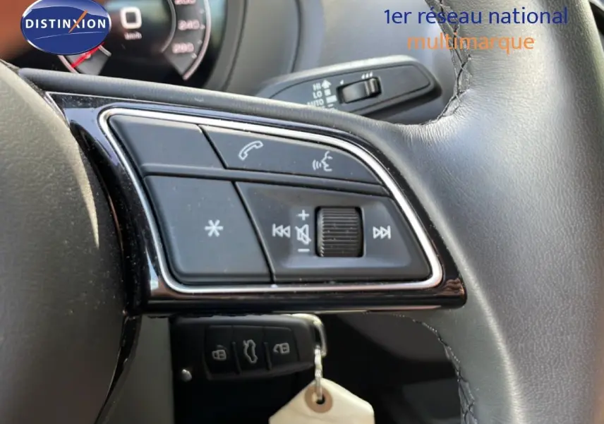 Gros plan sur les commandes au volant en cuir noir de l'Audi Q2 30 TDI S-Line, avec tableau de bord partiellement visible.