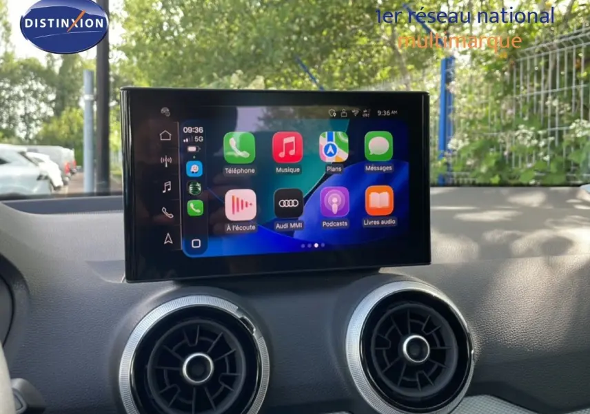 Écran tactile central de l’Audi Q2 30 TDI S-Line 2025, avec commandes multimédia et aérateurs ronds sur tableau de bord noir.