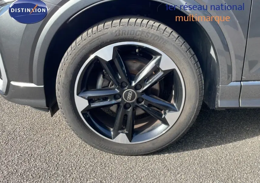 Gros plan sur la roue avant droite d’un Audi Q2 gris Manhattan avec jante alliage bicolore distinctive.