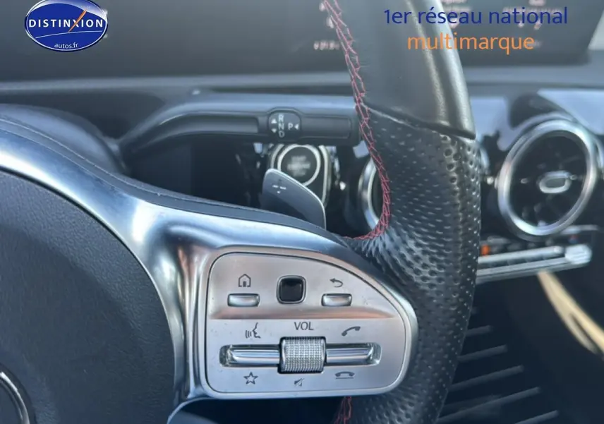 Gros plan sur la partie gauche du volant sport en cuir noir avec surpiqûres rouges de la Mercedes CLA 250 e AMG Line 2022.