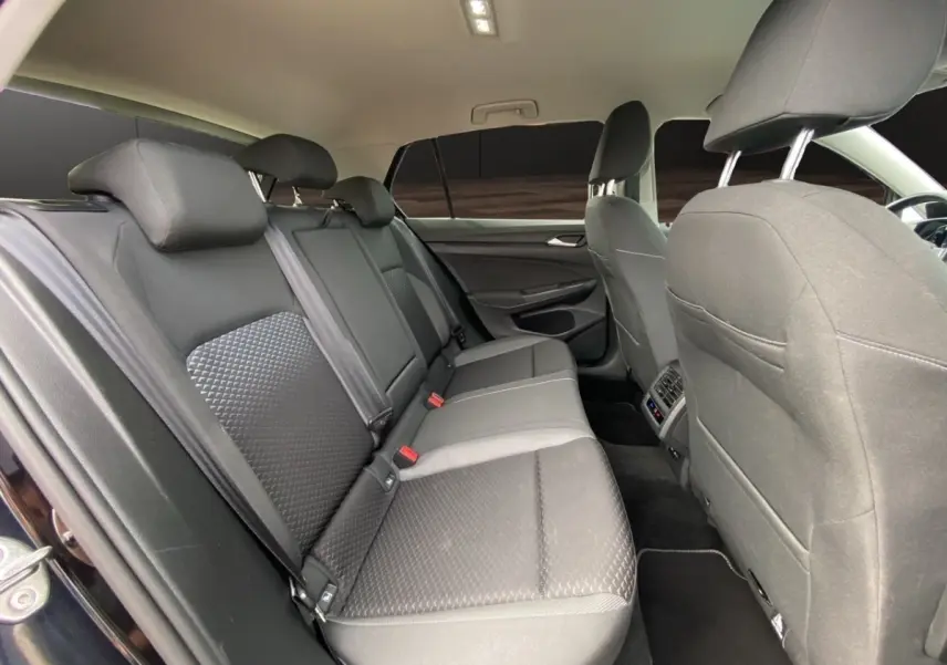 Vue intérieure arrière côté gauche de la Volkswagen Golf noire, montrant la banquette et les sièges avant en tissu gris.
