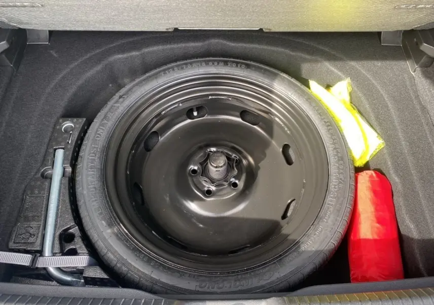 Vue plongeante sur la roue de secours noire et les accessoires de sécurité dans le coffre d'une Volkswagen Golf noire 2022.