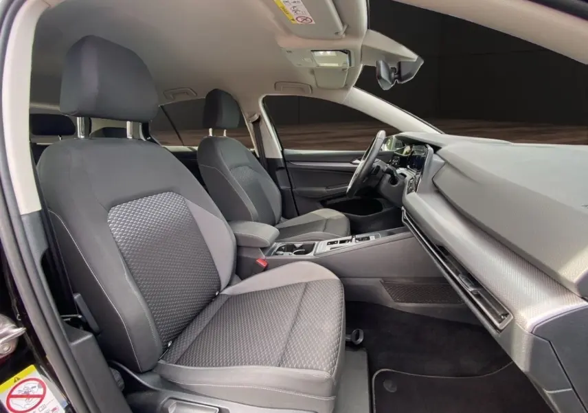 Vue intérieure avant droite de la Volkswagen Golf 1.0 eTSI noire, sièges tissu gris et tableau de bord moderne.
