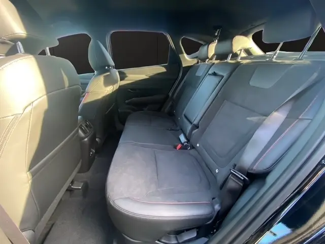 Vue intérieure arrière du Hyundai Tucson noir 2026, sièges en cuir noir avec surpiqûres rouges et accoudoir central.
