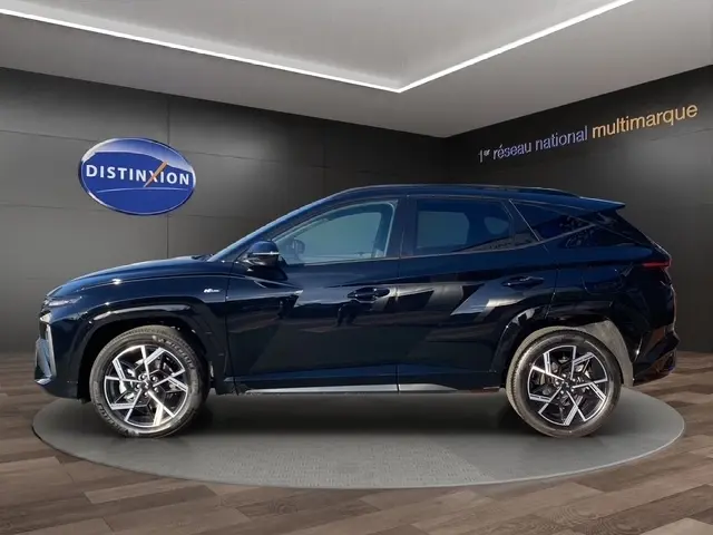 Vue latérale droite d’un Hyundai Tucson 1.6 Hybrid noir avec jantes alliage et toit noir brillant en showroom.