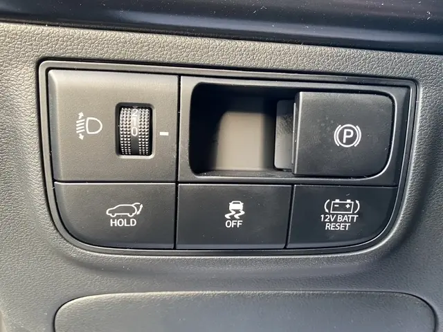 Gros plan sur les commandes intérieures noires du Hyundai Tucson 1.6 Hybrid 2026, avec bouton frein à main électrique et réglage phares.