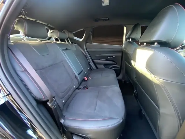 Vue intérieure des sièges arrière noirs du Hyundai Tucson 1.6 Hybrid 239 N Line Creative avec surpiqûres rouges et ceintures de sécurité.